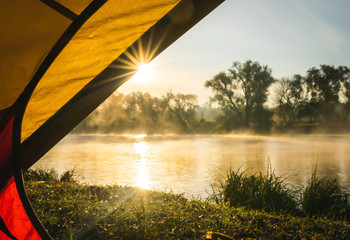Wall Mural - Sunrise sunflare peaking through the gap of the tent in a countryside of Ukraine and the river with mist nearby.