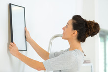 Young Woman Putting Frame On White Wall
