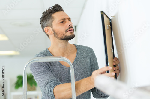 Fotomural male carpenter hanging picture frame on wall at home