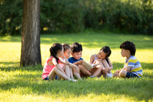 Happy Children Reading Book On Meadow