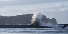 Rough Ocean Waves Crashing On Pier With Highlands As Background During Tide