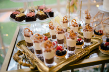 From Above Decorated Sweet Tasty Cheesecake Shooters On Golden Tray And Pink Flowered Cake On Glass Stand In Restaurant