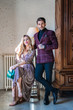 © Javier De La Torre/ADDICTIVE STOCK - Serious confident adult businessman in burgundy checkered jacket with magnificent pleased wife in shining dress looking away and enjoying view looking out window while standing beside wooden carved wardrobe and vintage floor lamp at home