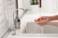 Woman Washing And Cleaning Her Hands Under Flowing Tap Water In The Sink Kitchen, Soft Focus, Potted Plant On Background. Hygiene Procedures Before Cooking Or Eating. 