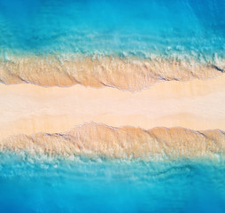 Aerial view of transparent blue sea with waves on the both sides and empty sandy beach at sunset. Summer holiday in Zanzibar, Africa. Tropical landscape with lagoon, white sand and ocean. Top view