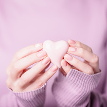 Beautiful Female Hands Holding Pink Heart On The Pale Violet Pink Background. Manicure With Pink Color Nail Polish, Nude Manicure With Fern Pattern