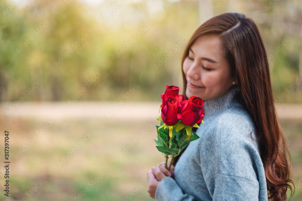 Closeup image of a beautiful asian woman holding and smelling red roses flower with feeling happy on Valentine's day - obrazy, fototapety, plakaty 