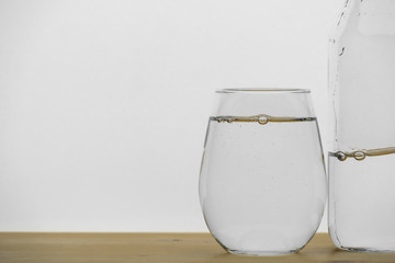 Wall Mural - Pure drinking water in the glass with bottle isolated on wooden table, white background