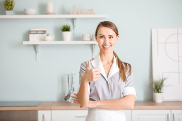 Poster - Portrait of beautiful chambermaid showing thumb-up in kitchen