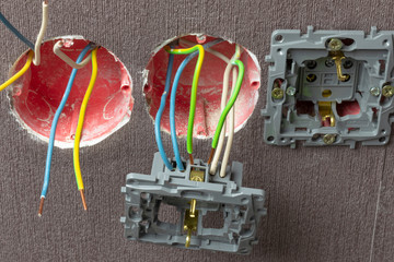 3 boxes of red color. Wall mounted. Of them stick out wires of different colors. one has a power outlet. Green, white, blue. Close-up.