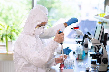 scientists in protection suits and masks working in research lab using laboratory equipment: microsc