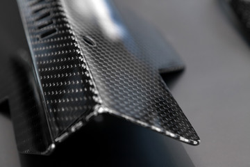 A close-up on a car exterior elements made from carbon fiber of interwoven black and gray color from heavy-duty yarns for the production of light and durable elements in industry. Tuning body parts.