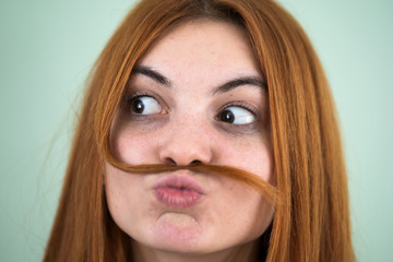 Wall Mural - Close up portrait of funny girl holding long red hair like a mustache under her nose.