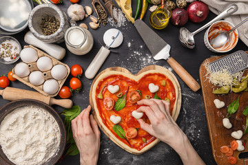 woman preparing a festive dinner for two in honor of Valentine's Day classic Italian pizza Margherita in the shape of a heart and mozzarella in the shape of a heart