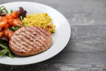 grilled hamburger with cereals and salad on white plate on ceramic background