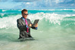 © PeskyMonkey - Shocked businessman trying to use his tablet computer in crashing waves on the shore of a tropical beach