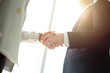 © iamchamp - business man and woman shaking hands at meeting room in office with window