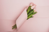 Fototapeta Tulipany - top view of tulip bouquet wrapped in paper swirl on pink background