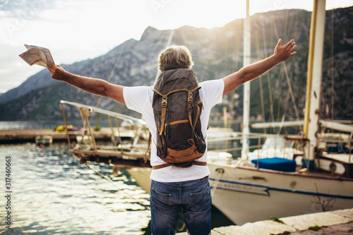 Cuadros en Lienzo Smiling tourist mature man standing with map and backpack near the sea