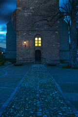 Wall Mural - Old church with illuminated window and lantern at dusk.