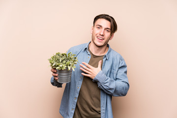 Young caucasian man holding a plant laughs out loudly keeping hand on chest.