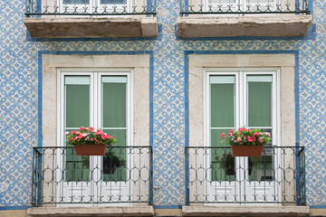 historic house facade with blue azulejos, two balconies and geranium flower pots, lisbon portugal