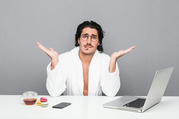 Wall Mural - Young handsome man working after a shower confused and doubtful shrugging shoulders to hold a copy space.