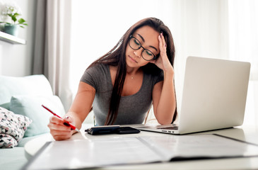 Desperate and worried asian woman calculating taxes bills at home