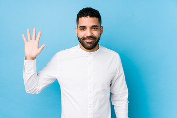 Wall Mural - Young latin man against a blue  background isolated smiling cheerful showing number five with fingers.