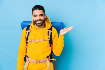 Wall Mural - Young arabian traveler backpacker man isolated showing a copy space on a palm and holding another hand on waist.