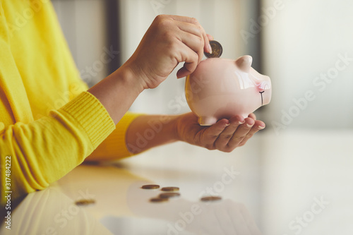 Cuadros en Lienzo Woman puts euro coin into piggy bank