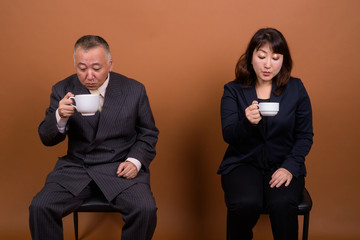 Mature Asian businessman and mature Asian businesswoman drinking coffee together