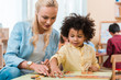 © LIGHTFIELD STUDIOS - Selective focus of teacher helping to african american kid with wooden game in montessori class