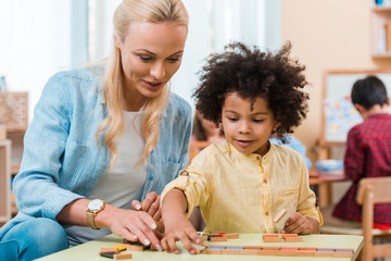 Selective focus of teacher helping to african american kid with wooden game in montessori class