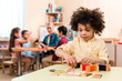 © LIGHTFIELD STUDIOS - Selective focus of african american kid playing educational game with teacher and children at background in montessori school