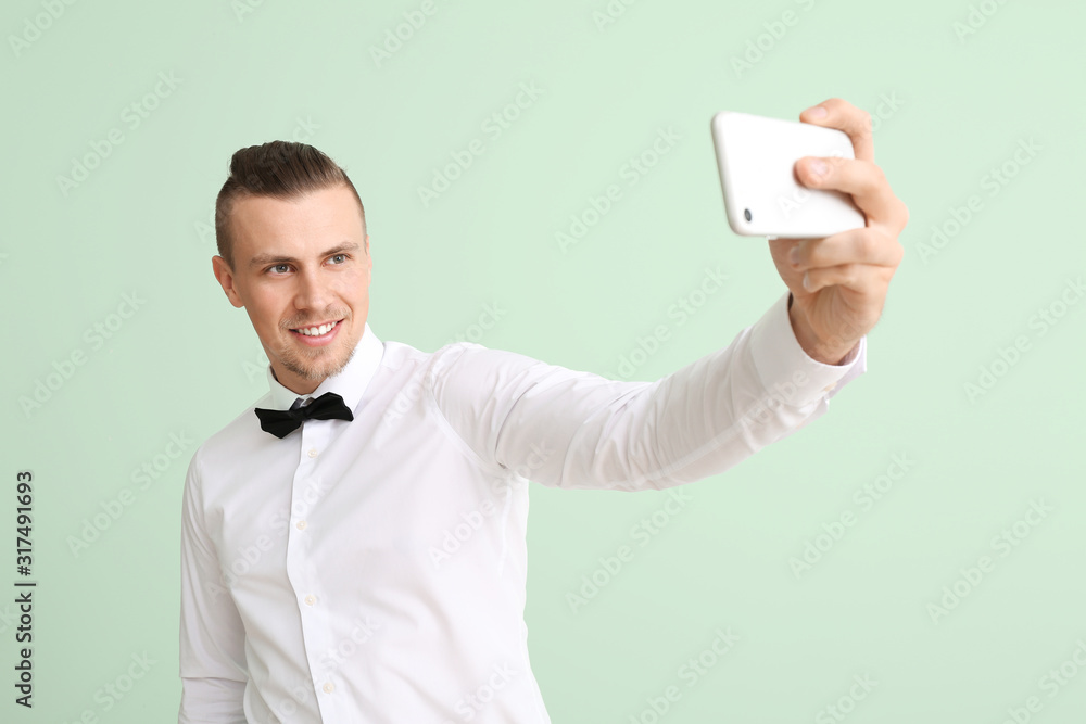 Handsome young man taking selfie on color background