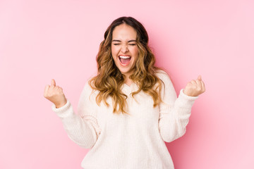 young curvy woman posing in a pink background isolated cheering carefree and excited. victory concep