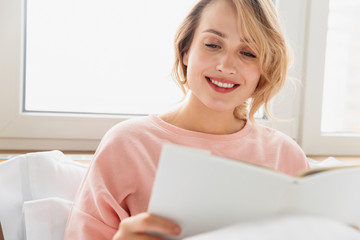 Canvas Print - Woman indoors at home lies in bed reading book.