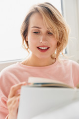 Canvas Print - Woman indoors at home lies in bed reading book.