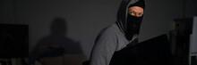 Portrait Of Male Thug Standing In Dark Room And Holding Expensive Televisor From Popular Company. Man Wearing Grey Hoodie And Black Mask. Stealth Robbery Concept