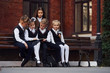© standret - School kids in uniform that sits outdoors on the bench with notepad