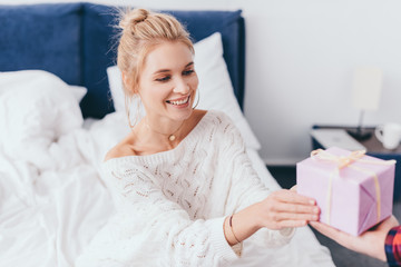 beautiful smiling woman taking gift box from man in bedroom