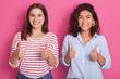 © sementsova321 - Image of curly haired brunette and attractive friend smiling sincerely, raising hands, making gestures, showing sign super, standing isolated over pink background in studio. Emotions concept.