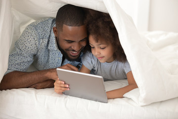 African father and daughter with tablet computer hiding under blanket