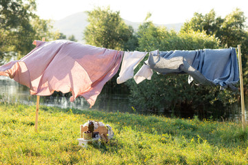 Pink and blue bedding sheet on forest background under the bright warm sun. Clean bed sheet hanging on clothesline at backyard. Hygiene sleeping ware concept.