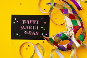 Festive, colorful mardi gras or carnivale mask and accessories over purple background. Party invitation, greeting card, venetian carnivale celebration concept. Flat lay, top view, copy space