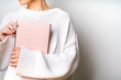 © PINKASEVICH - Close view of woman in white woolen sweater holding a book with empty pink cover in hands. Free space for your mock up of reading book concept background.