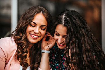 Two happy friends sharing a phone to listen music on line together in the street