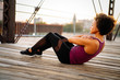 Woman in fitness attire doing sit ups on pedestrian bridge in city at sunset, eyes closed