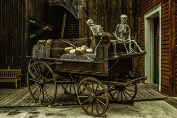 Sticker - Old wooden carriage with skeletons and pumpkins on it in a building